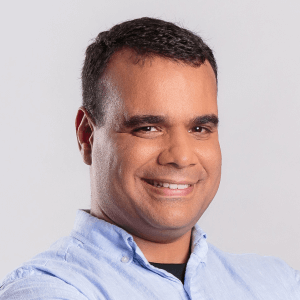 smiling man in blue shirt against light background, professional headshot with friendly expression and casual attire